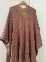 Ruana tejida en punto jersey, color negro con destellos brillantes de lurex. Presenta una etiqueta de cuero sintético con logo en la parte posterior.