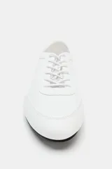 Zapatilla deportiva estilo blucher de color blanco, con cordones del mismo tono, pespuntes decorativos y suela plana con base negra.