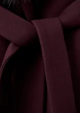 Abrigo largo de lana virgen color bordó, con diseño recto y cinturón tipo batín. Presenta cuello con solapas y un cuello de pelo sintético desmontable. Incluye bolsillos laterales y forro interior.