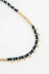 Collar corto con cuentas de metal dorado y cuentas de vidrio azul oscuro, con detalles de pequeñas borlas doradas en la parte frontal.