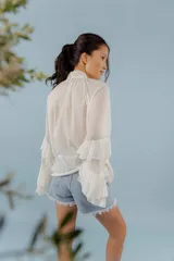 Blusa de algodón color blanco, con cuello alto y lazo frontal para atar. Presenta mangas largas con volados en los puños y un diseño holgado y romántico.