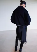 Chaqueta de corte amplio y estructurado en color negro, con cuello solapa, cierre frontal de cremallera metálica y bolsillos laterales discretos.