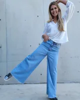 Pantalón de jean color beige, de corte recto y tiro alto, con ruedo deshilachado y cierre frontal con botón y cremallera.