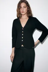 Chaqueta de punto color negro con escote en pico, manga tres cuartos y cierre frontal con botones dorados. Presenta un diseño con bajo asimétrico.