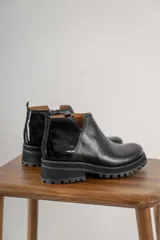 Botinetas negras con suela track, combinando cuero texturizado en la parte frontal y cuero charolado en la parte trasera. Diseño de caña baja con detalle de corte lateral.