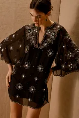 Vestido corto negro de tela transparente con mangas acampanadas y escote en V. Está completamente bordado con motivos florales y estrellas en lentejuelas y cuentas plateadas y verdes.