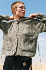 Chaqueta de punto de cuello redondo y manga larga, con textura jaspeada en tonos tierra y azul. Presenta cierre frontal con botones oscuros y dos bolsillos de plastrón en el delantero.