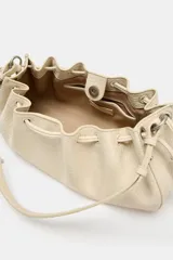 Mini bolso de hombro color crudo con diseño fruncido, textura granulada y cierre mediante cordones ajustables en los laterales. Cuenta con un asa fina de hombro.