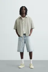 Bermuda de denim de algodón, color azul medio lavado, de corte ancho (baggy fit) y largo hasta la rodilla. Presenta cinco bolsillos y cierre frontal con cremallera y botón.