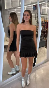 Vestido corto strapless negro ajustado al cuerpo, con diseño drapeado en los laterales y volado en el ruedo.