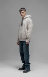Hoodie oversize de color beige, confeccionado en frisa premium. Presenta capucha ajustable con cordones, bolsillo tipo canguro frontal y puños con aberturas para pulgares.