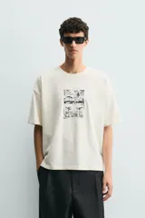 Camiseta de corte relajado color crudo, con cuello redondo y manga corta. Presenta un estampado gráfico en el frente con motivos de palmeras y paisajes en color negro.