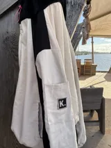 Campera oversize de gabardina combinada en colores crudo y negro, con cierre frontal y capucha de piel sintética negra. El interior está forrado en polar con diseño estampado.