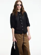 Camisa negra de algodón con cuello mao y botones frontales. Presenta mangas amplias y textura arrugada.