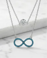 Collar doble de plata 925, compuesto por una cadena superior con dije de punto de luz y una cadena inferior con dije en forma de símbolo de infinito decorado con circonias turquesas.