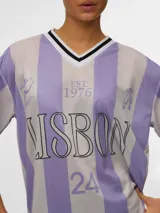Camiseta de estilo deportivo con diseño a rayas verticales en tonos lila y gris. Presenta cuello en V con detalles en blanco y negro, y estampado frontal con la palabra LISBON y el número 24.