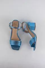 Sandalias de fiesta metalizadas color celeste, con taco cuadrado de 4 cm, tiras delanteras acolchadas y tira ajustable al tobillo con hebilla dorada.