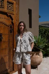 Short de tiro medio color blanco con estampado de flores negras y detalles de bordado. Presenta pierna holgada y bolsillos delanteros.