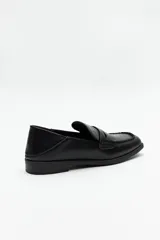 Mocasín de cuero sintético negro con punta cuadrada, detalle de costuras visibles en la capellada y taco bajo.