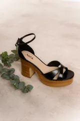 Sandalias color crema con tiras cruzadas y tobillera con hebilla dorada. Plataforma y taco de madera con diseño acanalado.