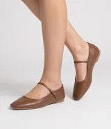 Zapatilla plana de cuero marrón estilo Mary Jane, con puntera cuadrada y tira fina con hebilla metálica dorada sobre el empeine.