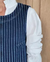 Chaleco de corte recto y largo a la cintura, confeccionado en denim con estampado de rayas verticales en tonos azul y blanco. Presenta cuello redondo y costuras visibles que definen su estructura.