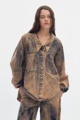 Camisa de denim oversize, con efecto acid wash en tonos marrones y negros, mangas abullonadas, cuello en V con solapa y bolsillos frontales con solapa.