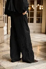 Pantalón de corte recto y holgado en color negro, con detalle de bordado floral tono sobre tono en la parte inferior de la pierna. Cuenta con bolsillos laterales y cierre frontal con botón.