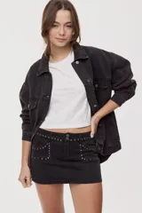 Minifalda de denim negro, tiro medio y corte ajustado, con bolsillos delanteros decorados con tachas metálicas y doble botón en la cintura.
