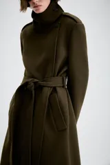 Abrigo de corte recto confeccionado en mezcla de lana, color verde oscuro. Presenta cuello subido, cierre frontal cruzado con botones, mangas largas con trabillas en los hombros, bolsillos delanteros y cinturón ajustable del mismo tejido.