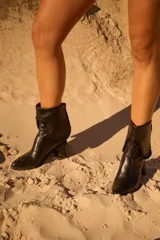 Botas cortas de cuero marrón oscuro con punta afilada, taco ancho y detalle de costuras decorativas.