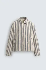 Cazadora de hombre de corte relajado, color beige claro con rayas verticales en azul oscuro con efecto desgastado o estampado. Presenta cuello solapa, manga larga, bolsillos de vivo en cadera y cierre frontal con botones a presión.