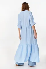 Vestido camisero largo de lino italiano color celeste, de corte relajado, con mangas caídas, jareta ajustable en la cintura, cierre frontal de botones y bajo con volado fruncido.