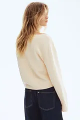 Saco corto de punto suave en color beige, con diseño de hombros caídos y escote amplio ribeteado. Cuenta con mangas largas y cierre frontal de botones con efecto carey.
