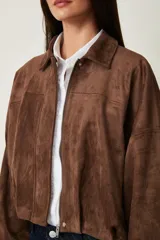 Campera de gamuza marrón, de corte oversize con hombros caídos, cuello camisero, cierre frontal de cremallera y puños y dobladillo elásticos.