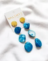 Aros colgantes con base dorada circular y piedras irregulares nacaradas en tonos turquesa y blanco.