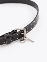 Cinturón de cuero vacuno negro con efecto gastado, adornado con mini tachas metálicas a lo largo de la lonja, hebilla metálica y dijes colgantes en forma de llave.