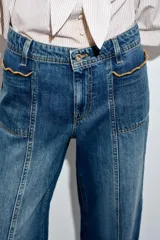 Jeans de tiro alto con corte culotte y pernera ancha. Presenta bolsillos de plastrón en el frente con detalle de pespuntes decorativos en forma de onda y costuras verticales a lo largo de la pierna. Cierre frontal con cremallera y botón metálico.