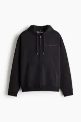 Campera canguro de felpa negra con cierre frontal, capucha con cordón ajustable, hombros caídos y bolsillos tipo kermesse. Cuenta con el logotipo de la banda Guns N' Roses bordado en el pecho en color rojo.