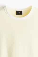 Remera de algodón en punto liviano, con diseño boxy de corte holgado. Presenta cuello redondo acanalado y ribetes en contraste en cuello y mangas, con hombros caídos y bajo recto.