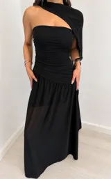 Vestido largo negro de diseño elegante, con cuerpo drapeado estilo strapless, falda larga con capa exterior transparente y estola o bufanda integrada al cuello.