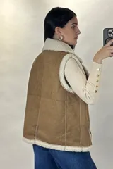 Chaleco tipo gamulán color marrón con interior y bordes de corderito sintético color crema. Presenta cierre frontal y bolsillos laterales con cremalleras metálicas, además de detalles de tiras de cuero sintético.