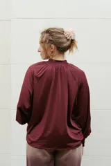Blusa de satén color negro, con cuello alto fruncido y mangas largas abullonadas con puños elásticos.