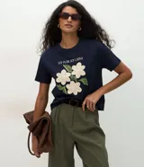Remera de algodón color azul marino, con cuello redondo y manga corta. Presenta un estampado frontal con texto y flores con apliques bordados en relieve.