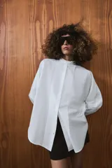 Camisa amplia de algodón con cuello redondo, manga por debajo del codo con puño y bajo asimétrico con aberturas laterales. Presenta cierre frontal con botones ocultos por solapa.