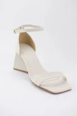 Sandalias color crema con tira delgada sobre los dedos, pulsera al tobillo con hebilla y taco geométrico.