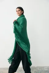 Ruana tejida en lana merino extrafina con detalles de lino y viscosa, color verde. Presenta un diseño de tejido artesanal con flecos en los bordes, ideal para usar de forma envolvente.