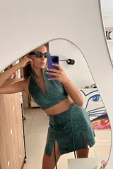 Top corto de cuero ovino color verde azulado con textura vintage, cuello halter y espalda descubierta con cierre de hebilla metálica. Combina con falda a juego.