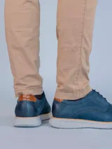 Zapato de estilo casual tipo derby en color azul marino, confeccionado en cuero con detalles de perforaciones decorativas tipo brogue. Cuenta con cordones al tono, detalle en cuero color suela en el talón y suela de goma flexible color gris claro con tecnología de amortiguación.