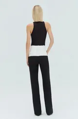 Pantalón de sastrería bicolor, de corte recto y holgado, con cintura alta y trabillas. Cuenta con un diseño en contraste donde la pretina y la parte superior presentan un bloque en color blanco, mientras que el resto de la prenda es negro. Posee bolsillos delanteros y traseros, y cierre frontal con cremallera, botón y corchetes.